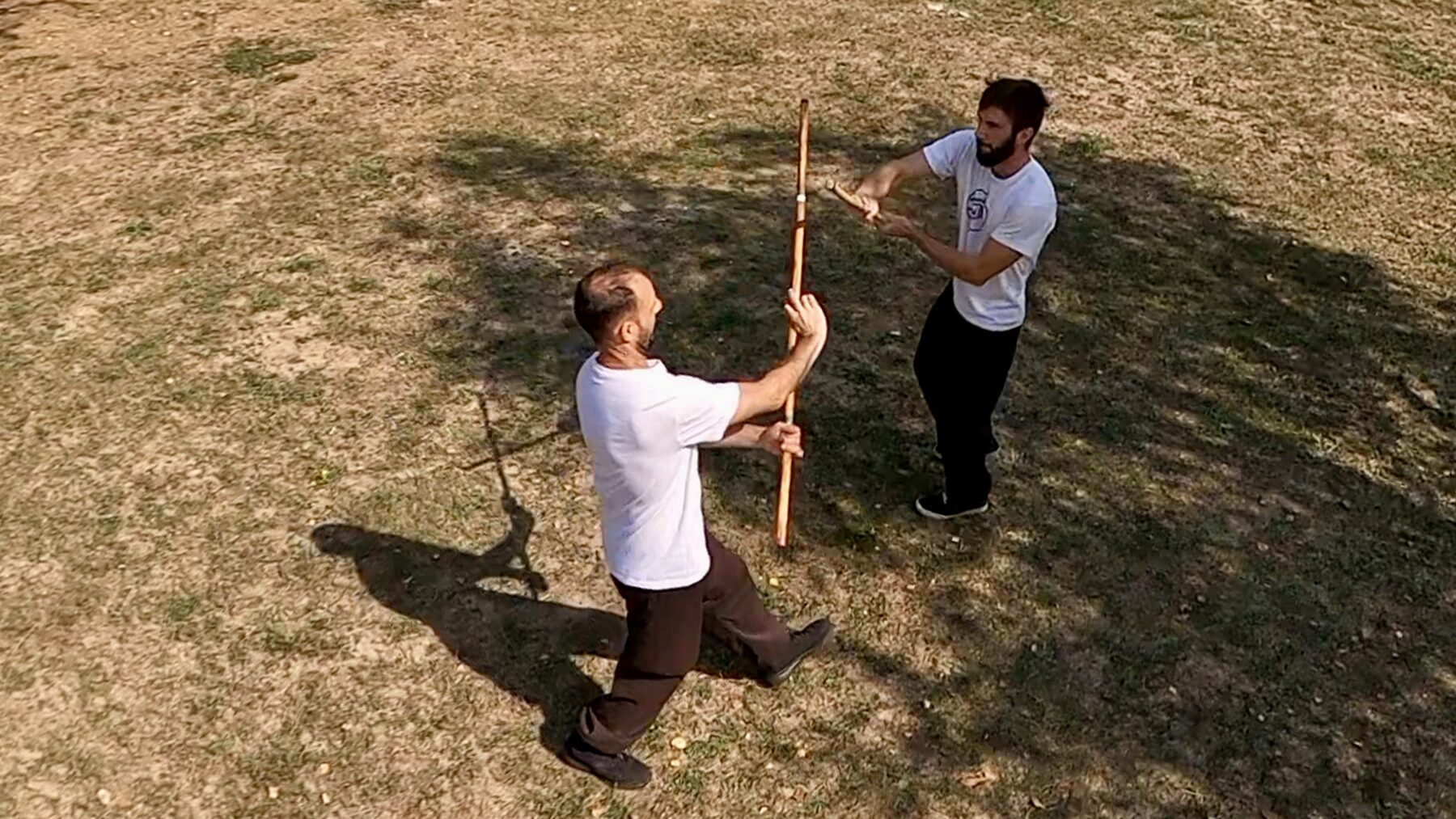 Deux pratiquants de Mo Kwon, bâton vertical, se font face sur une pelouse