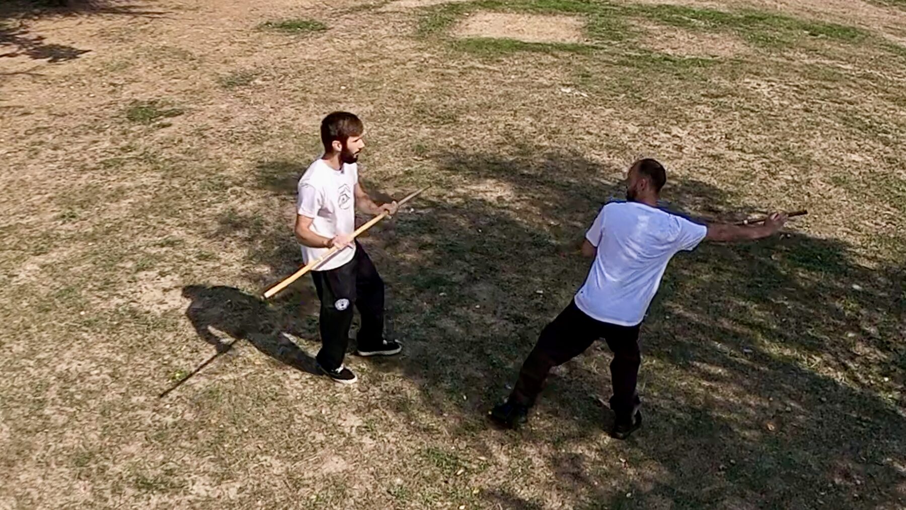 Deux pratiquants de Mo Kwon : l'un tient le bâton à hauteur de hanche, l'autre tend le bras en fente