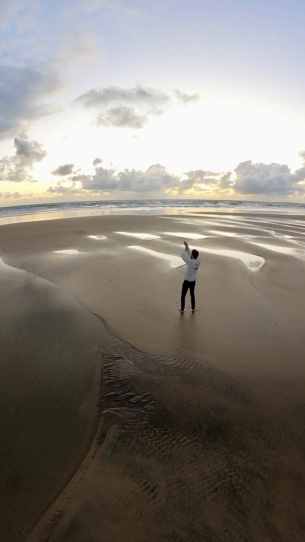 Pratiquant de Qi Gong, bras levés, sur une plage au coucher du soleil