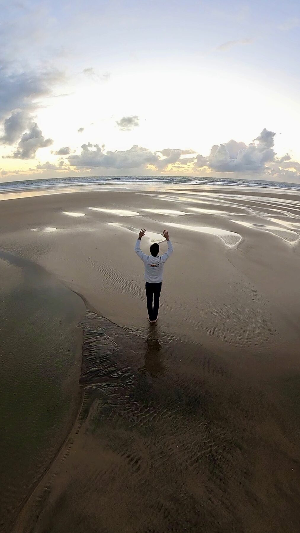 Pratiquant de Qi Gong, bras levés, face à la mer à marée basse