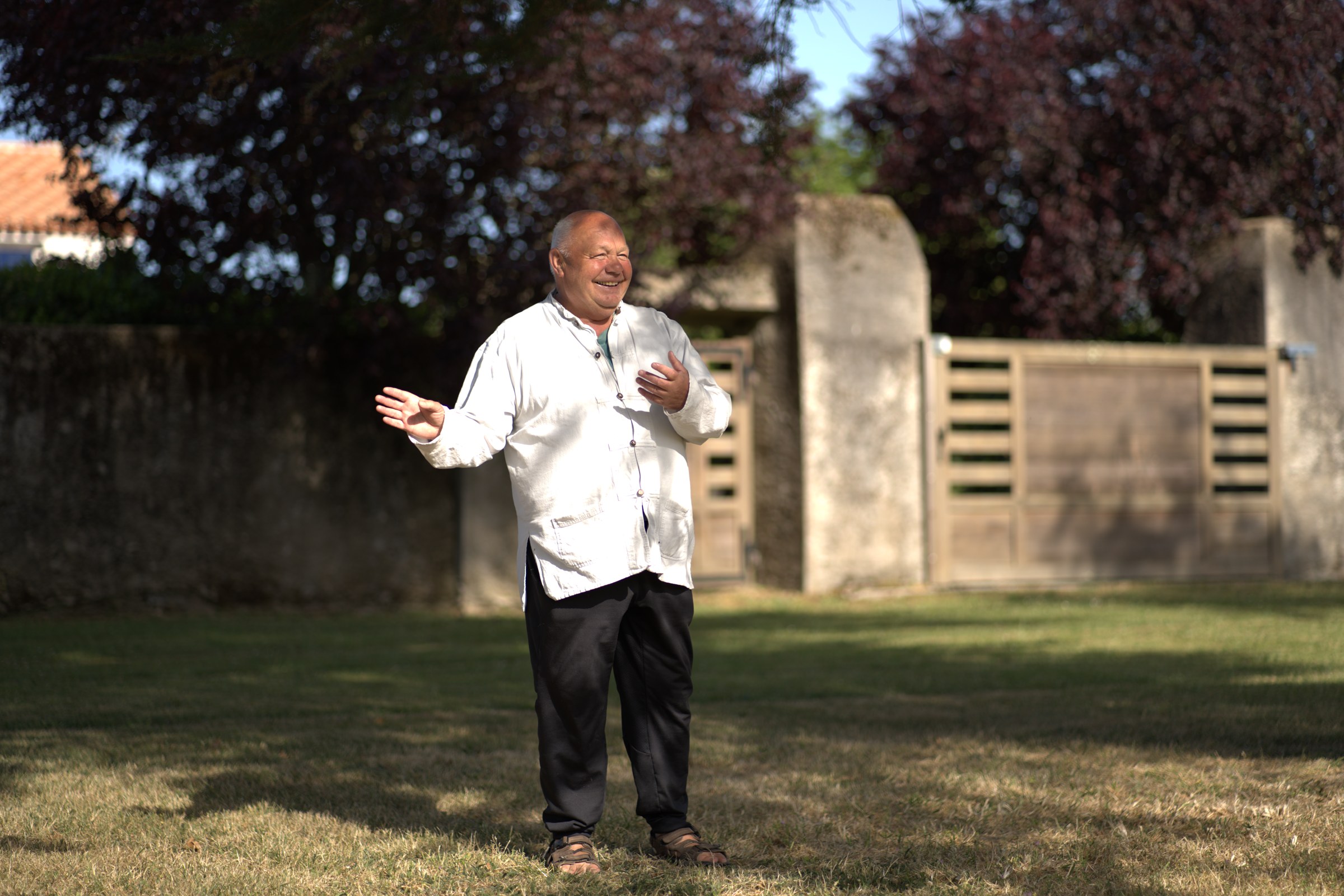 Thierry Potin, souriant, les bras ouverts sur une pelouse devant un portail en bois